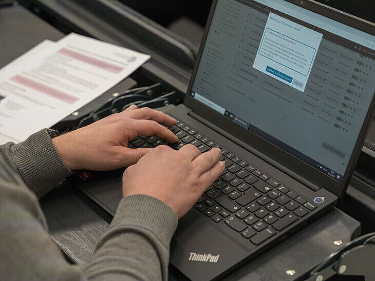 Symbolbild digitale Prüfungen. Auf dem Bild ist ein Student im Hörsaal mit einem Rechner und Prüfungsunterlagen zu sehen. ster, 2022