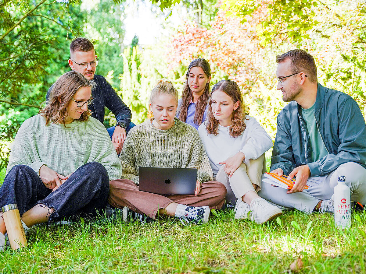 Studierende sitzen auf einer Wiese