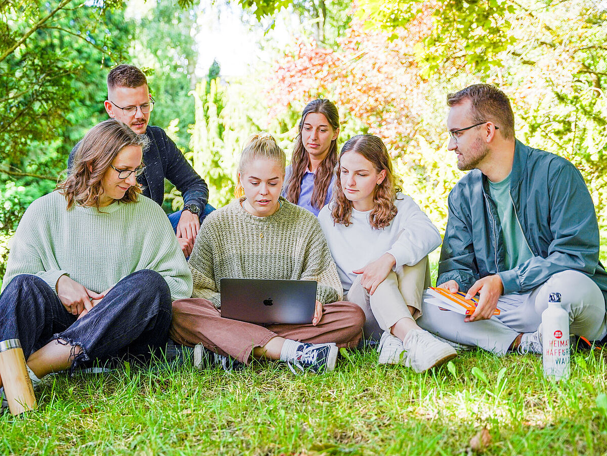 Studierende sitzen auf einer Wiese