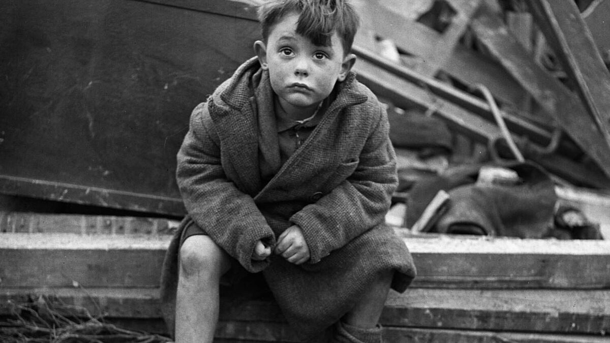 Symbolfoto Kriegskind Ein Kind sitzt in den Trümmern des Zweiten Weltkriegs und blickt fragend in die Kamera.