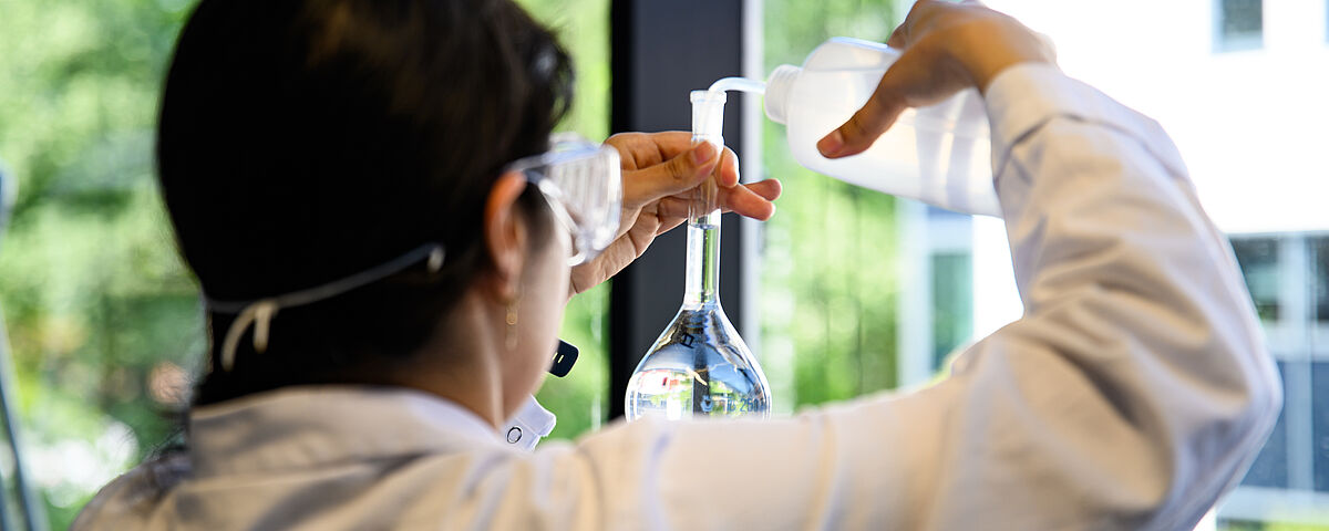 Eine Wissenschaftlerin füllt etwas in etwas in einen Erlenmeyerkolben um.