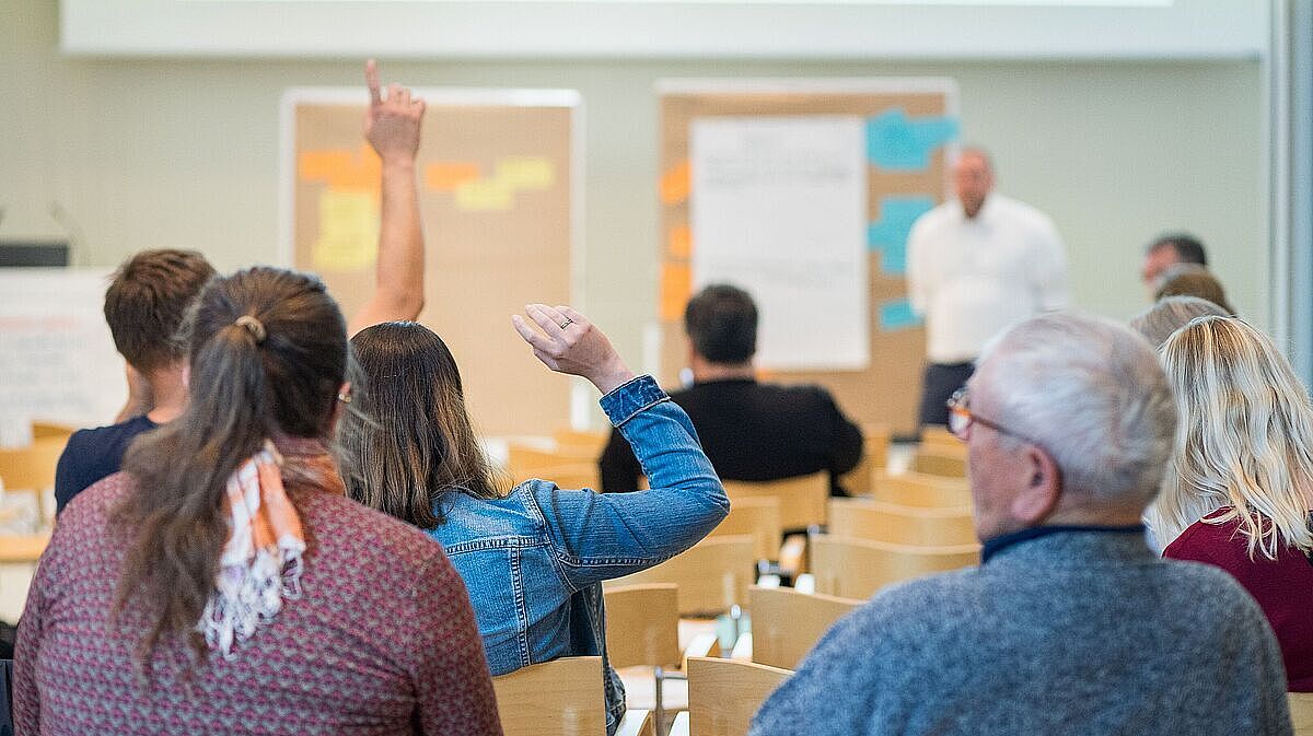 Mehrere Personen melden sich in einem Seminar zu Wort.