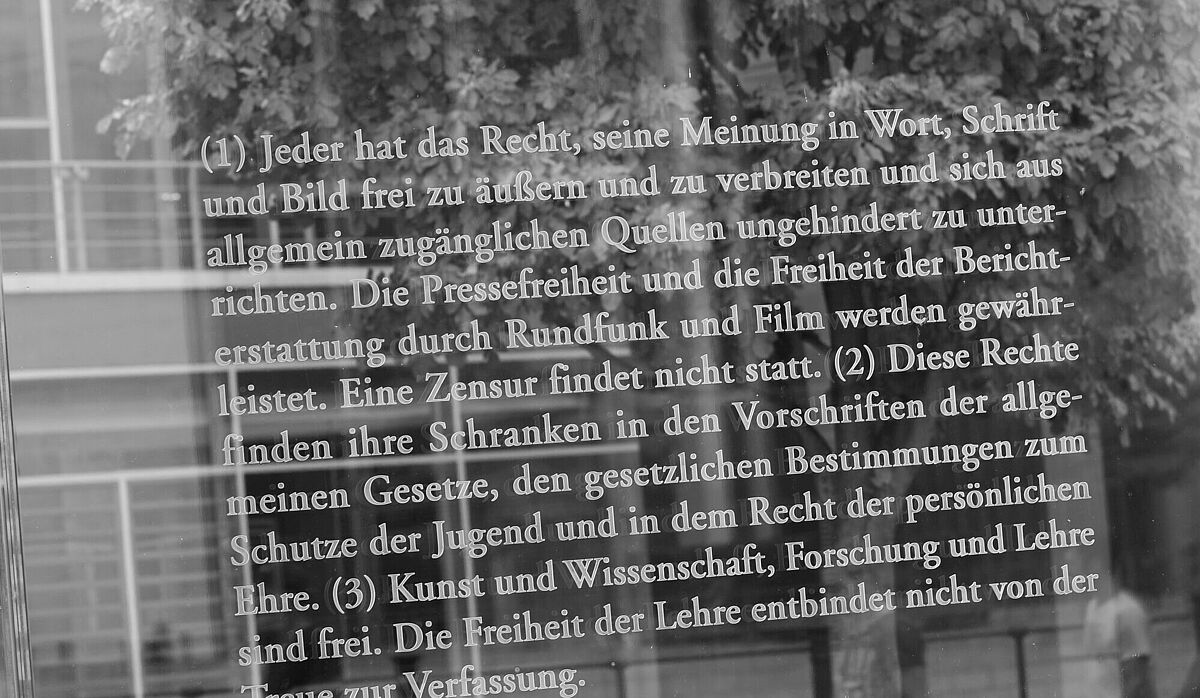 Auf einer Glasscheibe steht der Artikel 5 des Grundgesetzes mit weißer Schrift geschrieben.