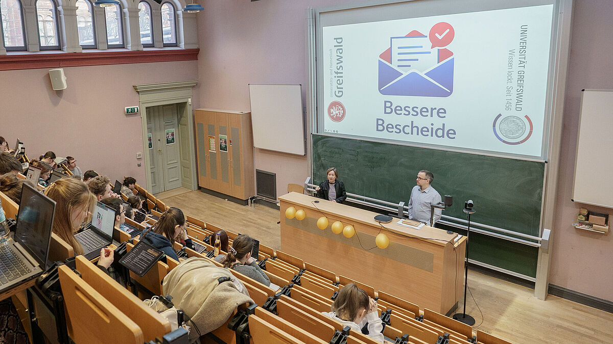 Mehrere Personen sitzen im Hörsaal und hören den Dozierenden zu.