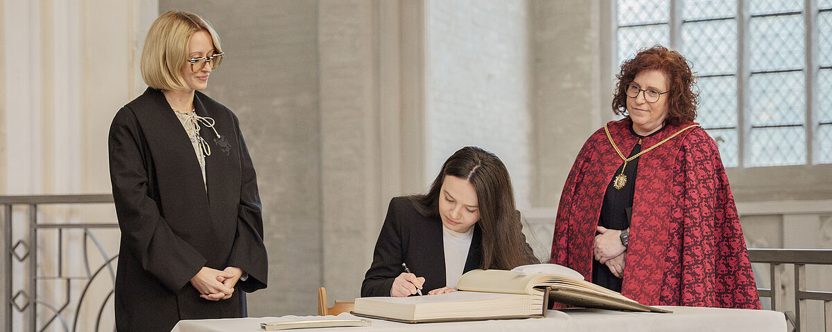 Eine junge Frau schreibt sich in ein altes großes Buch in einer alten Kirche ein.